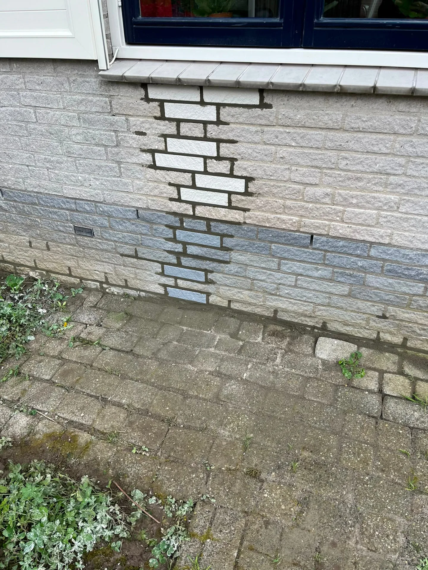Inboetwerk met nieuwe stenen in een lichte gevel onder de vensterbank