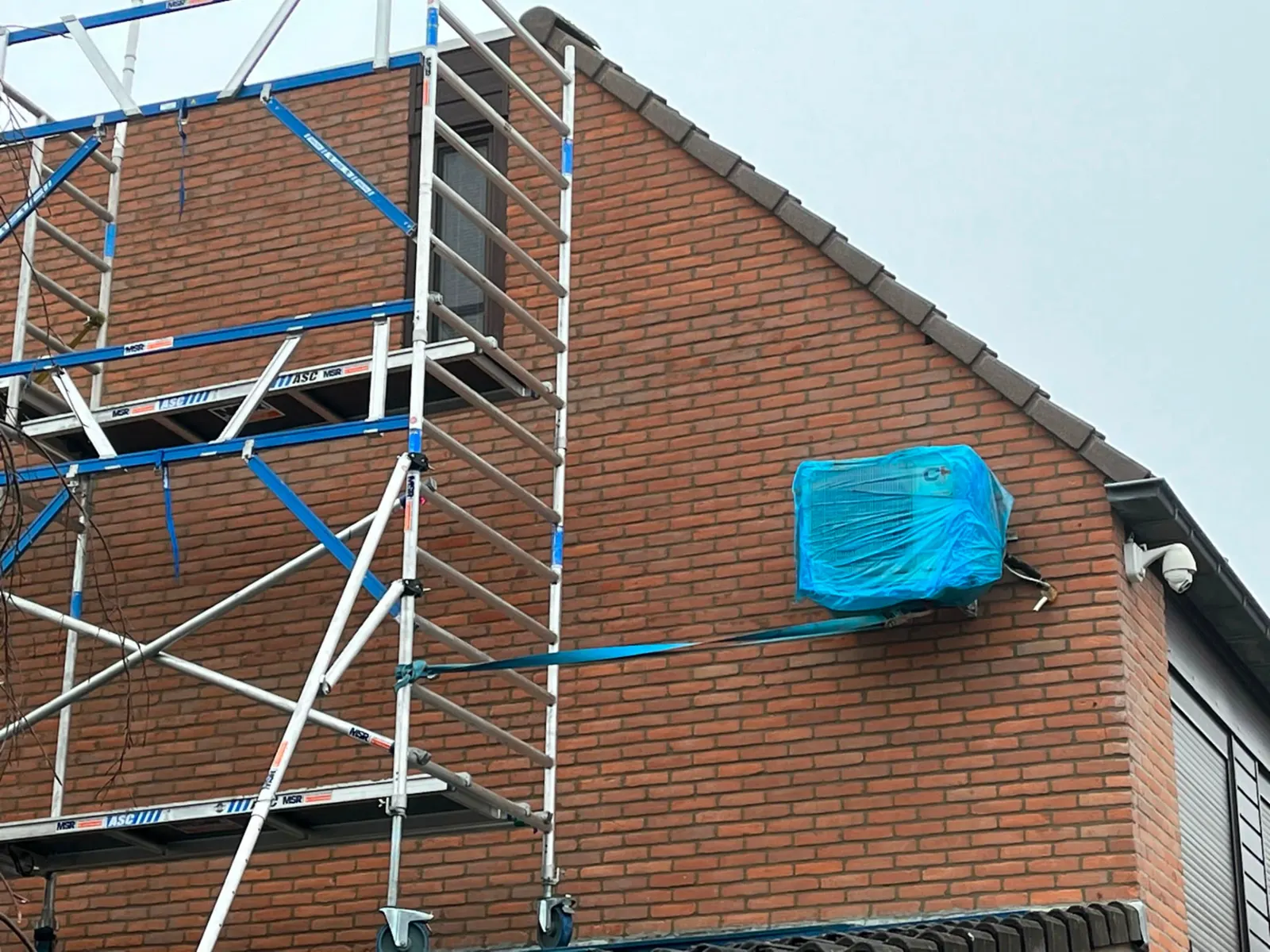 Steigerwerk langs een bakstenen topgevel tijdens gevelrenovatie