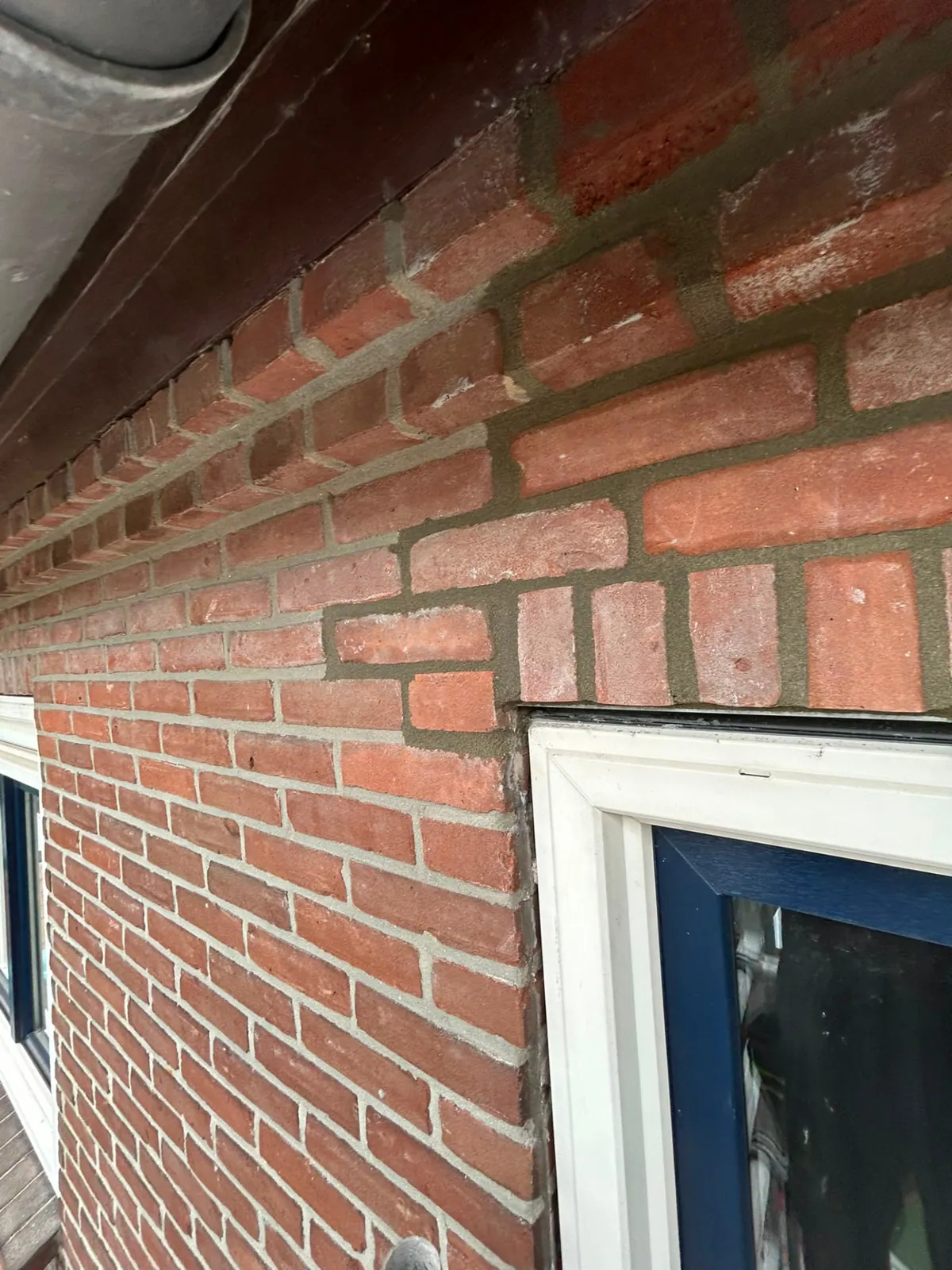 Vernieuwd voegwerk in een rode bakstenen gevel boven een raamkozijn
