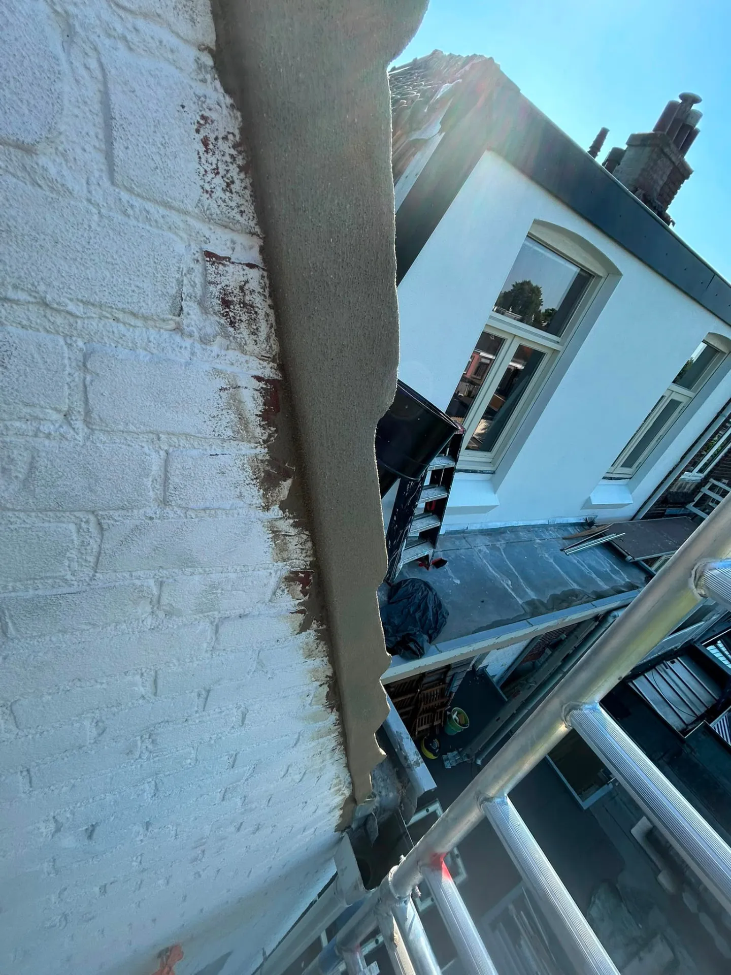 Herstelde en gestucte dakrand op een witte gevel tijdens renovatie
